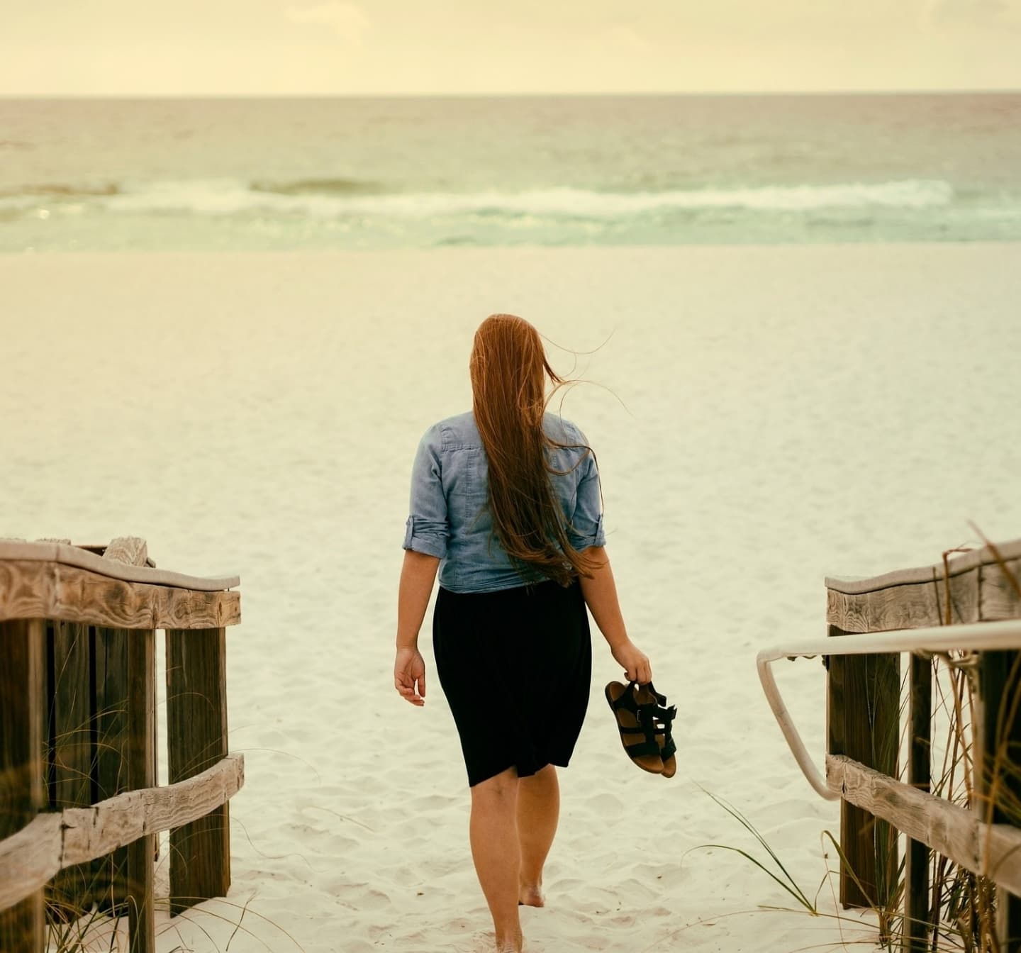 Women walking on a wooden bridge towards the sea - in between worlds.