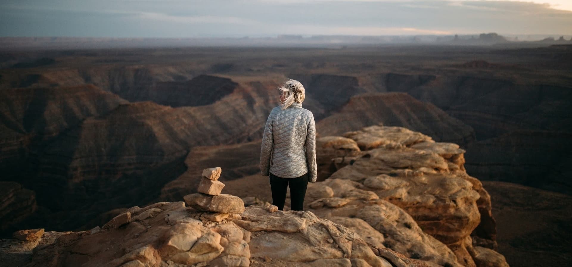 A woman standing on a mountain top at facing a mountain landscape.