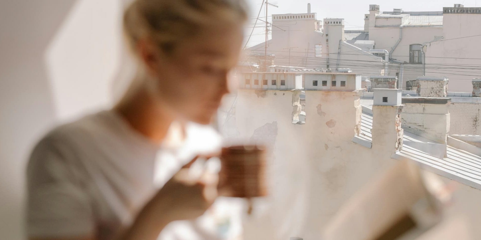 A woman sits in a window with a coffee cup, a city skyline behind her, lost in her own thoughts
