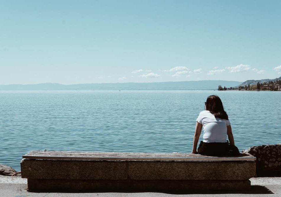 Women siting alone by the sea reflecting and looking at the horizon